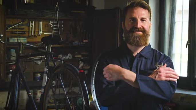 一位成功的穿着整齐的英俊的大胡子大师时髦的肖像，自行车专家，在他的车间修理自行车，车轮，车架，扳手。