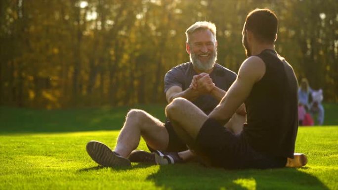 快乐的父亲和一个儿子坐在草地上聊天。慢动作