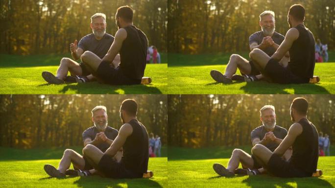 快乐的父亲和一个儿子坐在草地上聊天。慢动作