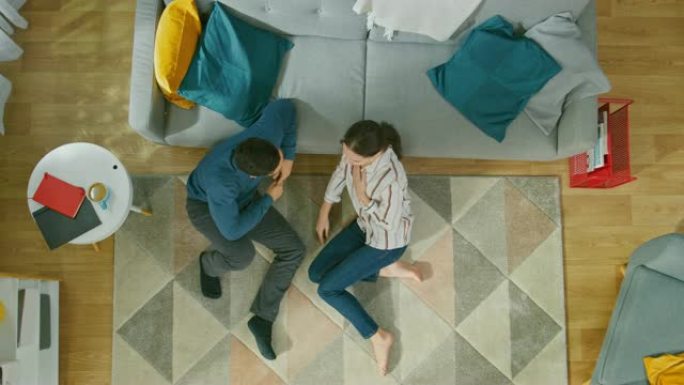 年轻夫妇坐在地板上聊天。他们进行了情感对话。舒适的客厅，配有现代室内地毯、沙发、椅子、桌子、书架、植