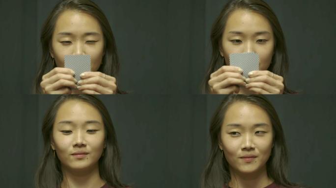 年轻的亚洲女人玩扑克，微笑着看着她的牌。