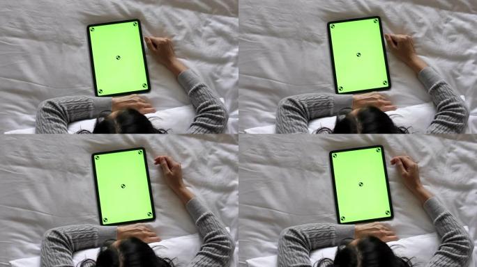 年轻女子在家中床上使用带绿屏的数字平板电脑，顶视图