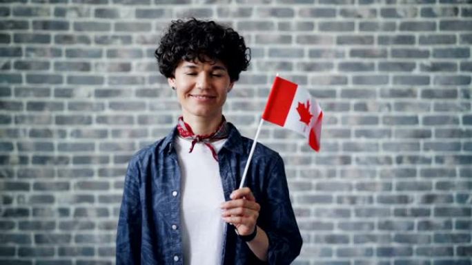 在砖块背景上举着加拿大国旗的可爱学生的慢动作肖像