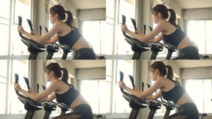 固定自行车上有吸引力的亚洲女性在健身房锻炼。慢动作。医疗保健、运动和运动概念。
