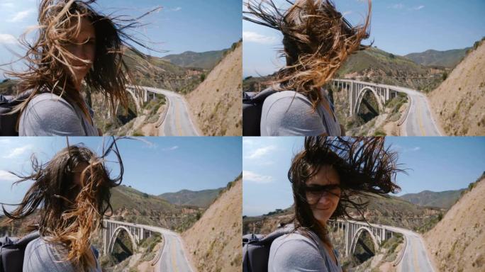 迷人的年轻女子，留着飞舞的头发，在大苏尔比克斯比溪桥令人惊叹的阳光视景点看着相机。