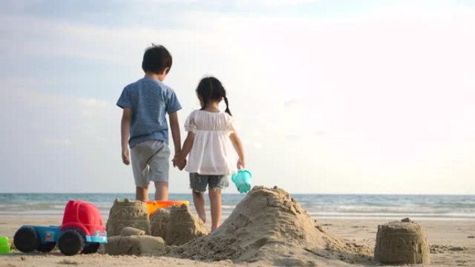 小女孩和她的兄弟一起在沙滩上玩耍，建造沙堡。慢动作。家庭、假期和旅行概念。