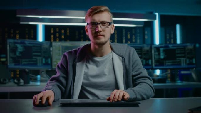 软件开发人员/黑客的肖像戴着眼镜坐在办公桌前，在数字身份网络安全数据中心的计算机上工作。黑客攻击或编