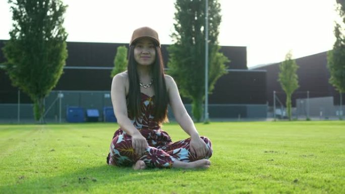 年轻的亚洲妇女坐在休闲服装的草地上