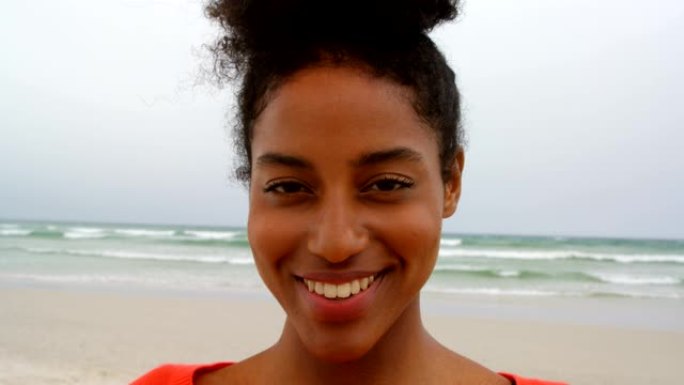 年轻黑人女子微笑着看着4k海滩上的相机的前视图