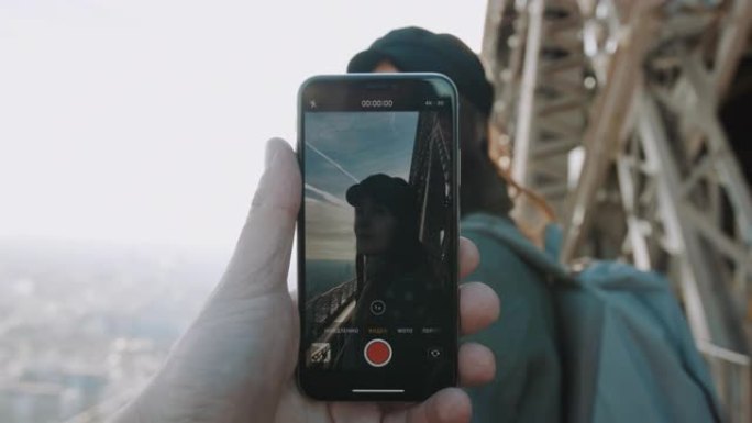 男性正在拍摄智能手机视频，该视频是快乐微笑的女人在埃菲尔铁塔上摆姿势。浪漫概念慢动作。