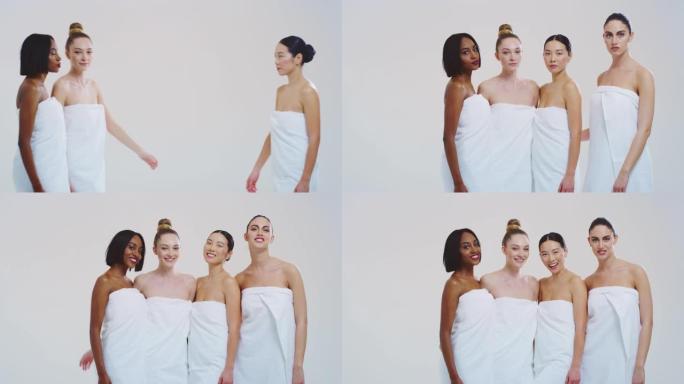 不同种族的美丽年轻女性的慢动作，完美结实苗条的身体，穿着白色浴巾，在相机里玩乐大笑，孤立在白色背景上