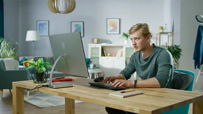 专注的年轻人坐在办公桌前在个人电脑上工作的肖像。背景舒适的客厅。