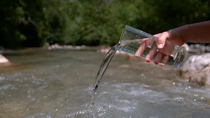 慢动作无法识别的人将玻璃中的水倒入山河中