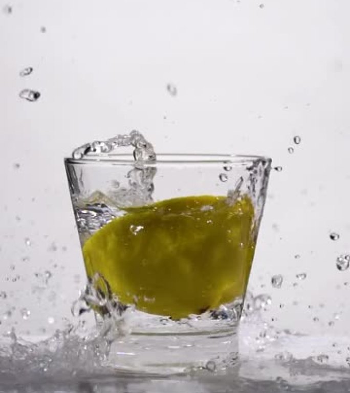 柠檬切片溅入玻璃的垂直射击和慢动作