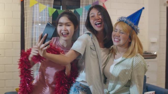 一群亚洲女性在家里聚会，女性使用手机在社交媒体上制作vlog自拍照，晚上在客厅一起跳舞。年轻朋友庆祝