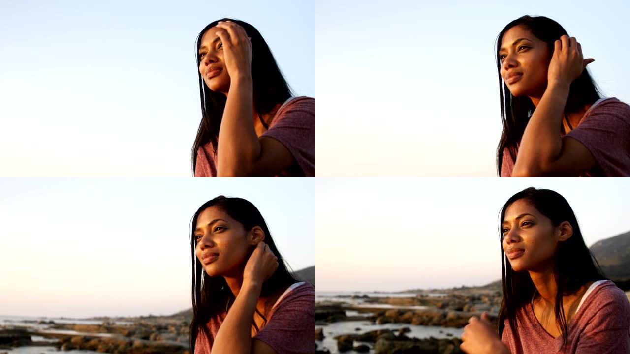 日落4k时，体贴的混血女人坐在海滩上的岩石上