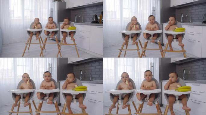 亚洲婴儿三胞胎坐在厨房的高脚椅上吃香蕉