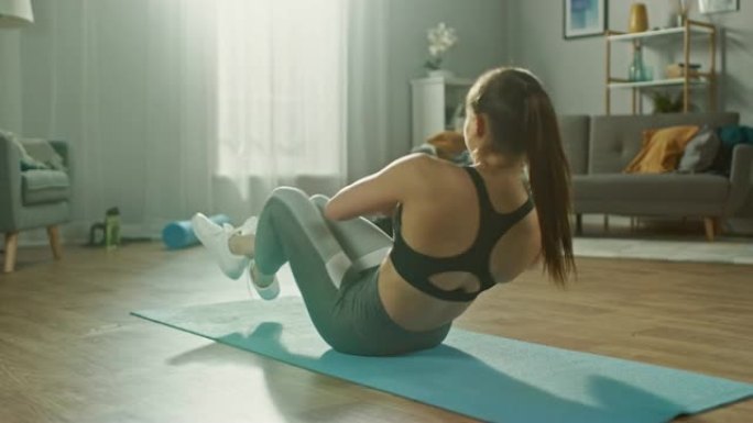 穿着运动上衣的美丽自信强壮健身女性正在她明亮宽敞的公寓里做腹部锻炼，室内简约。