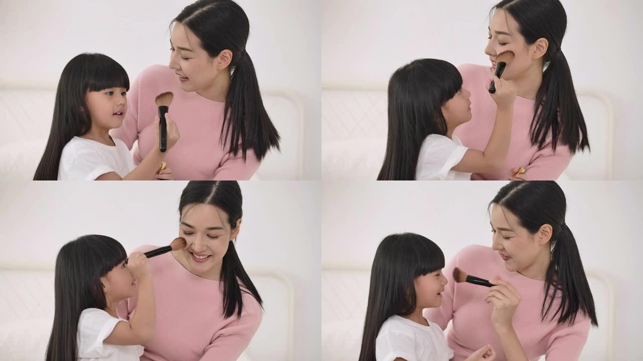 可爱的小女儿用化妆刷化妆妈妈。幸福的爱的家庭。