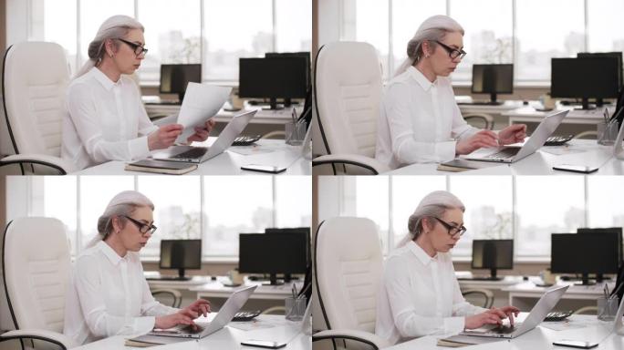 周末在办公室工作的灰发商务女士在笔记本电脑上工作