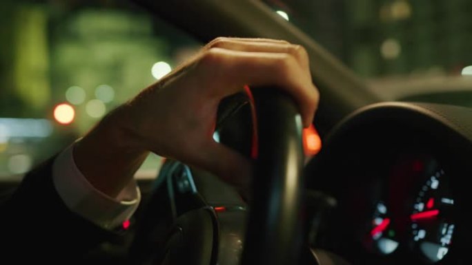 夜间在城市中心驾驶现代汽车的年轻商人手的慢动作特写。