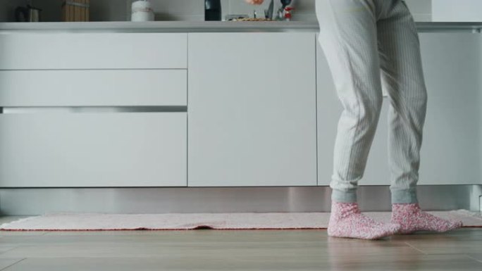穿着睡衣的年轻女子的慢动作特写早上在厨房喝咖啡后听音乐跳舞