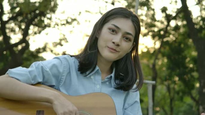 年轻迷人的亚洲女人在夏日公园弹吉他。具有幸福情感概念的女人。慢动作。