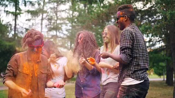 快乐的青年男女慢动作在聚会上跳舞，扔粉末涂料，然后在明亮的尘土中大笑。幸福和假期概念。
