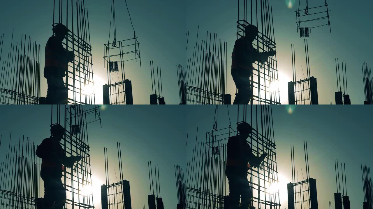 一名建筑商在日落背景上的钢筋上编织杆。