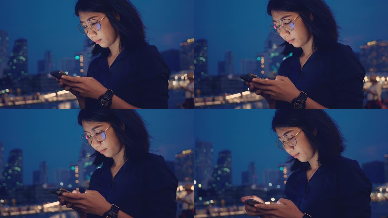 年轻的亚洲妇女在曼谷市通过电话发短信。