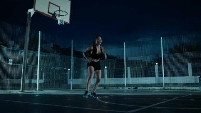 美丽精力充沛的健身女孩做步法跑步训练。她正在一个有围栏的室外篮球场里锻炼身体。居民区雨后的夜间录像。