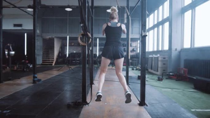 意志力和动力，镜头跟随年轻的运动金发女子向前跳跃，在健身房慢动作训练。