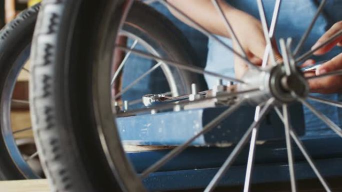 十几岁的男孩使用扳手拧紧螺栓上的螺母，将车轮固定在他的赛车卡丁车上，通过车轮的辐条可以看到近距离的中