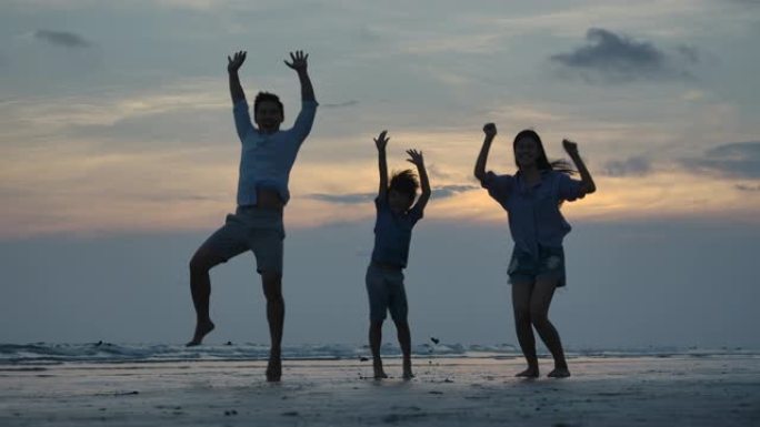 幸福的家庭在日落背景的海滩上跳跃的剪影，慢动作。家庭、自由和旅行理念。