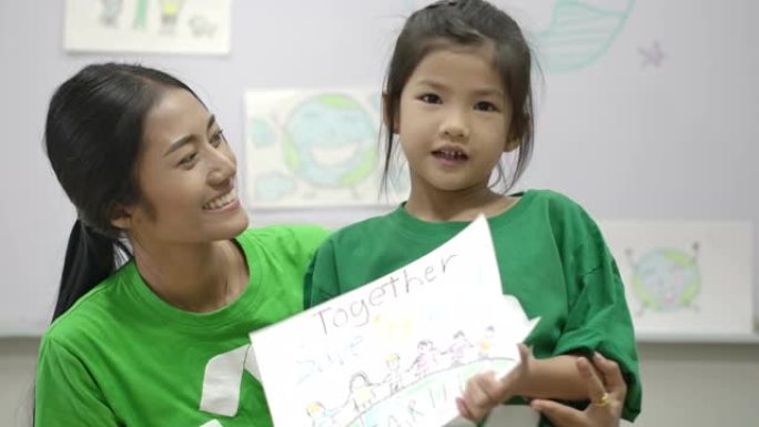 小女孩和老师的肖像，穿着绿色生态t恤，拿着她关于拯救世界项目的图纸。志愿者、自然和教育理念。