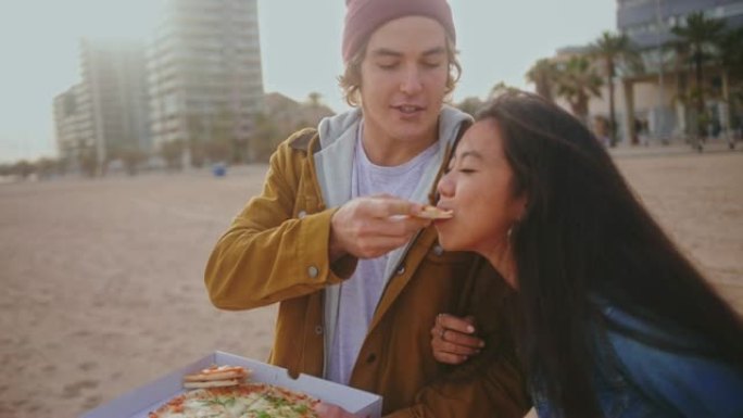 年轻的多种族夫妇在城市海滩上吃披萨很开心
