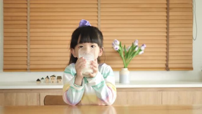 可爱的小女孩正在家里的餐桌上喝牛奶。