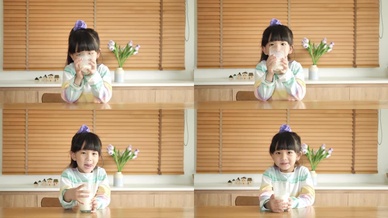 可爱的小女孩正在家里的餐桌上喝牛奶。