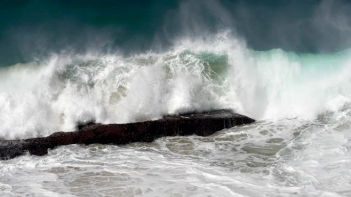 强大的巨大绿松石海浪压在岩石海岸上，变成白色泡沫。慢动作镜头