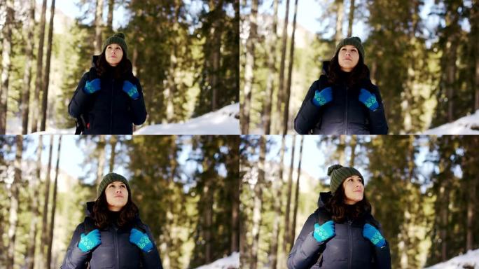 一个女孩休息放松，看着他面前的雪山，抱着他的背包在雪地里散步后徒步旅行。