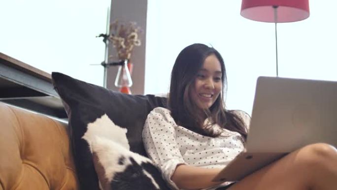 亚洲妇女在沙发上使用笔记本电脑