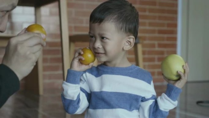 4k慢动作镜头亚洲小男孩拿着橙色和苹果，微笑着充满幸福的现代阁楼房子生活，家庭和童年概念