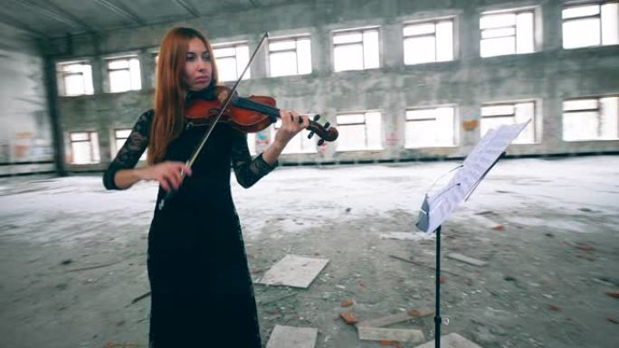 专业小提琴手在废弃建筑的大房间里按音符演奏。
