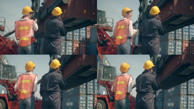 两名集装箱码头员工在航运港口彩色货物集装箱堆前工作