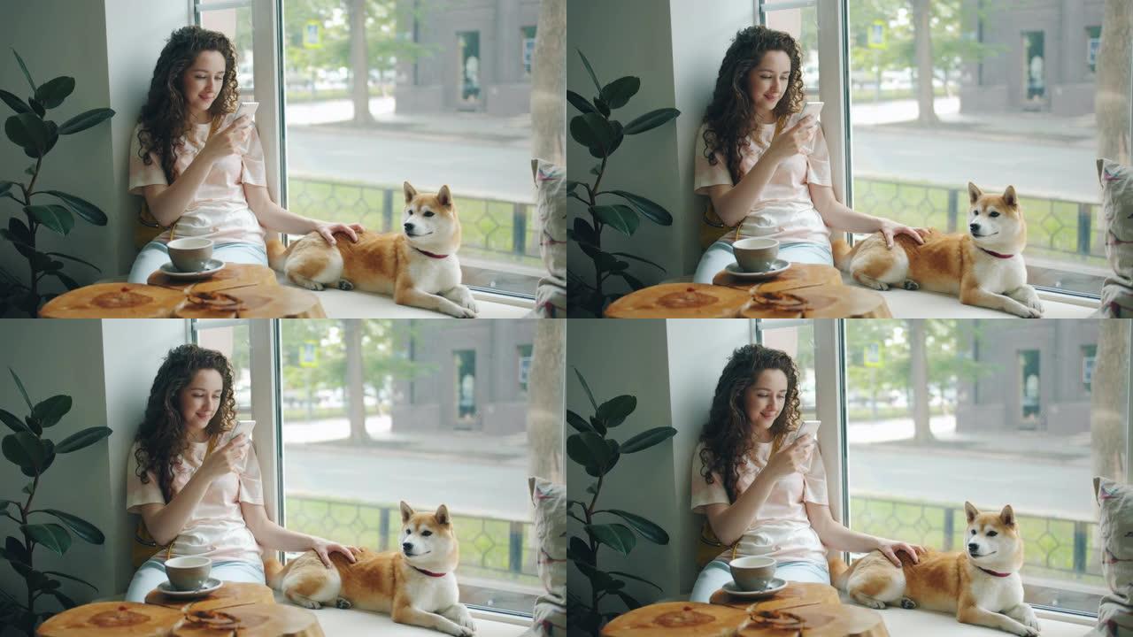 迷人的女人用智能手机坐在咖啡馆的窗台上，带着小狗
