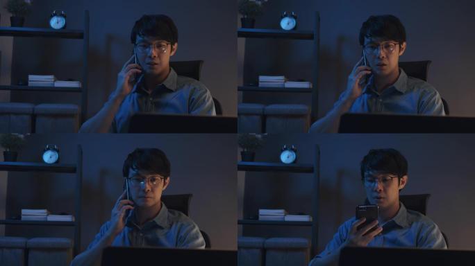 迷人的亚洲男子与他的团队在智能手机上交谈，并在晚上在家庭办公室使用笔记本电脑。商人坐在家里面对冠状病