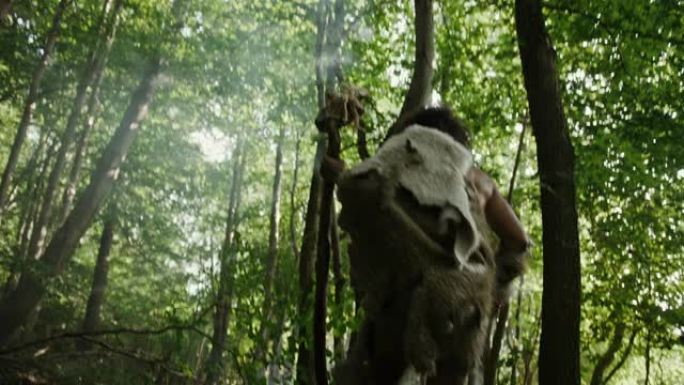 穿着动物皮的原始穴居人手持石尖斧头，探索史前森林以寻找动物猎物。尼安德特人去丛林打猎。向下倾斜射击