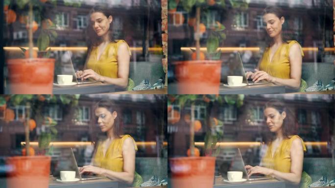 年轻女性自由职业者在咖啡馆用笔记本电脑工作，在桌子上微笑