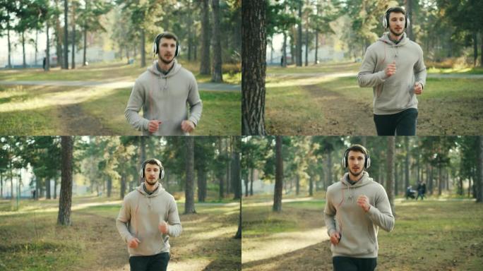多莉拍摄了长着胡子的好男人，戴着耳机在公园里跑步，在阳光明媚的秋天听音乐。现代科技和体育理念。