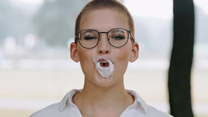 戴眼镜的迷人年轻女子咀嚼和吹泡泡糖